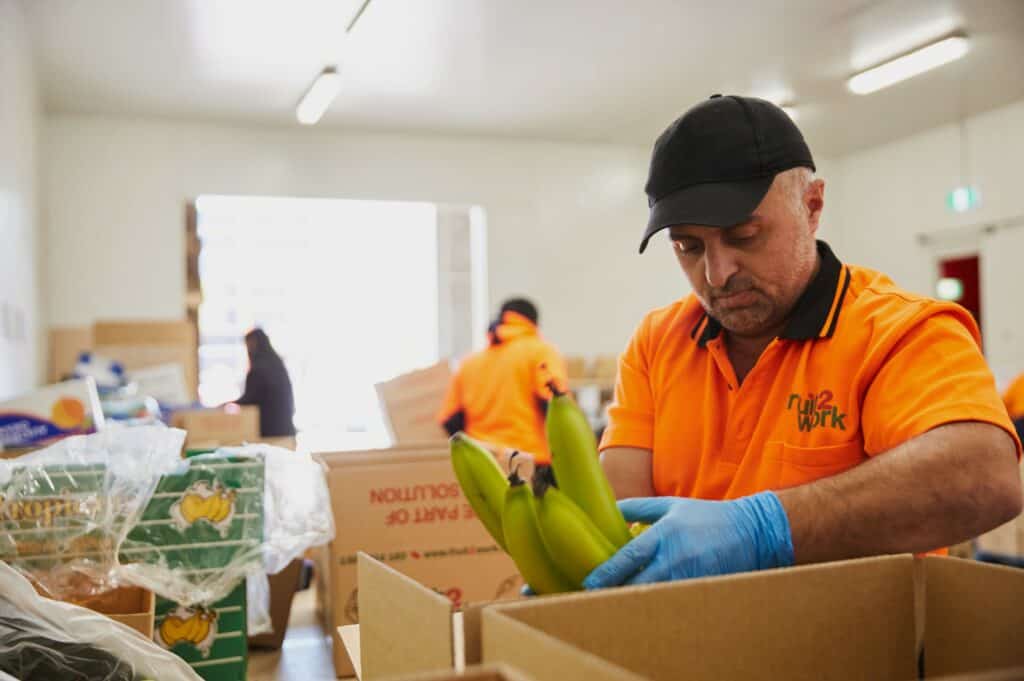 A man wearing high-visibility workwear packs fruit in a cardboard box